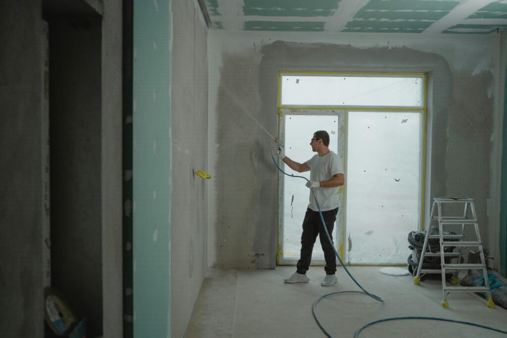 A man sprays paint on a wall while renovating an indoor room with professional equipment.
