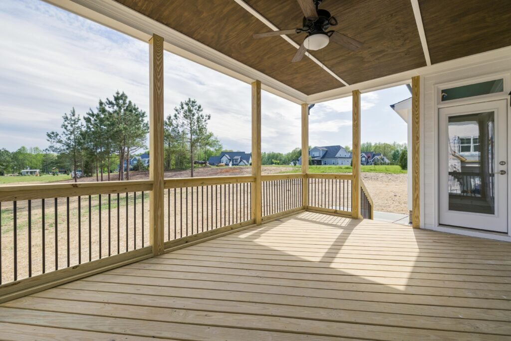 A bright wooden porch with ceiling fan and glass door, overlooking a grassy area.